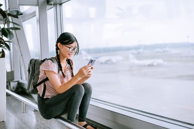 Tween girl looking at smartphone at airport while waiting for flight leggins