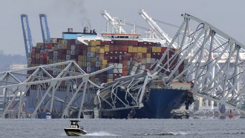 A boat moves past a container ship as it rests against wreckage of the Francis Scott Key Bridge on Tuesday, March 26, 2024, as seen from Pasadena, Md. 