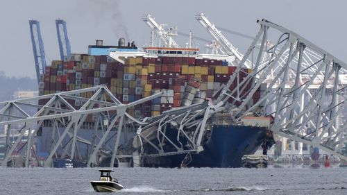 A boat moves past a container ship as it rests against wreckage of the Francis Scott Key Bridge on Tuesday, March 26, 2024, as seen from Pasadena, Md. 