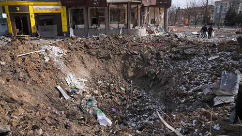  People walk past a crater from the explosion in Mira Avenue (Avenue of Peace) in Mariupol, Ukraine, Sunday, March 13, 2022. 