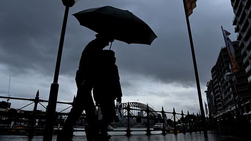 A man and child walk along Circular Quay shielding themselves from the rain with their umbrella. Sydney, NSW. 19th July, 2022. Photo: Kate Geraghty