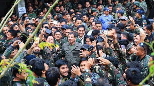 Rodrigo Duterte poses for selfies with many soldiers at once. (AAP)
