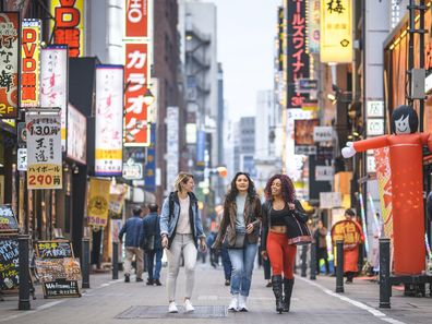 female tourists walking together through Shinjuku in Tokyo at dusk.
