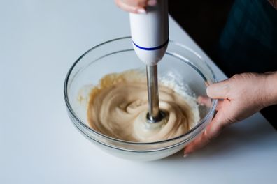 A chef's skilled hands blend homemade mayonnaise with olive oil using a blender.