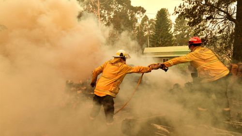 Firefighters hose down a burning woodpile during a bushfire in Werombi, 50km south west of Sydney, Friday, December 6, 2019.