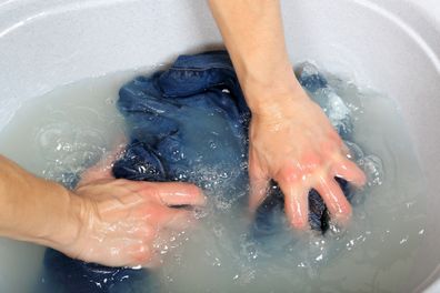 woman washing a pair of jeans by hand in plastic tub