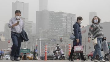 People wearing face masks walk across an intersection during a dust and sandstorm in Beijing, Thursday, April 13, 2023. Many areas in northern China were blanketed with floating sand and dust on Thursday, and a sandstorm was expected to sweep through parts of Inner Mongolia. (AP Photo/Mark Schiefelbein)