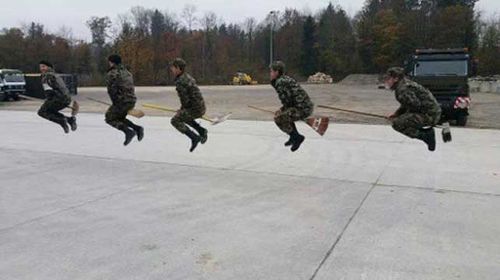 Photo of Swiss soldiers pretending to fly broomsticks. 