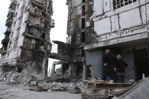 I residenti locali si trovano accanto agli edifici danneggiati durante i pesanti combattimenti a Mariupol, in un'area controllata dal governo della Repubblica popolare di Donetsk, nell'Ucraina orientale, venerdì 13 maggio 2022.  