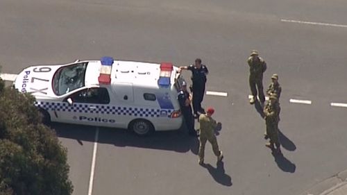 Police speak with military personnel outside HMAS Cerberus. (9NEWS)