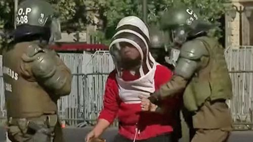 A beekeeper is apprehended by police at the protest in Chile.