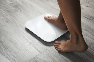 Female leg stepping on floor scales, close-up. Woman and weighing scales at home. Diet, healthy lifestyle, loss weight, slim concept.