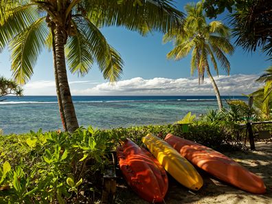 A tropical island holiday, a beach with palm trees and sea kayaks on the south pacific island Kingdom of Tonga.