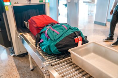 A colorful backpack and a small suitcase end up on a roller conveyor after being scanned in an X-ray machine for safety. A plastic container for it. 3/4 length shot.