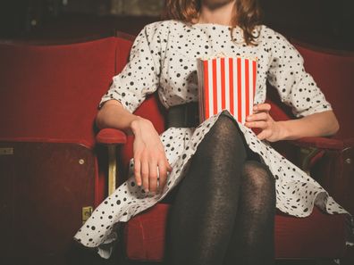 Young woman sitting alone in a cinema with a bucket of popcorn.