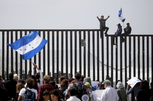 Central American migrants sit on top of the border wall in an attempt to seek asylum. (AAP)