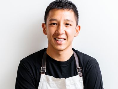 Brendan Pang poses in a black shirt and white apron