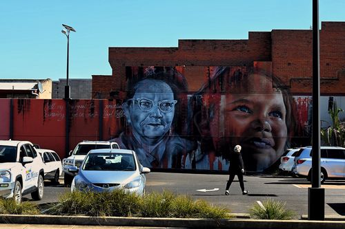 A woman walks across a car park in front of a mural on the side of a building on Talbragar Street in Dubbo, NSW. (Photo: Kate Geraghty)