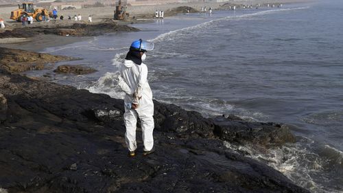 Workers stand on a rock covered with oil at Cavero beach in Ventanilla, Callao, Peru, Unusual high waves that authorities attribute to the eruption of the undersea volcano in Tonga caused the spill on the Peruvian Pacific coast as a ship was loading oil into La Pampilla refinery.