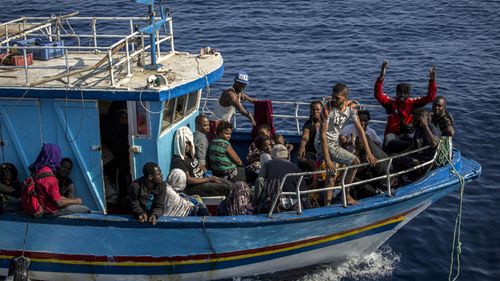 A migrant waves as others rest on their boat as it sails close to the Open Arms aid boat on Sunday June 30, 2019. A Spanish humanitarian group says its rescue ship spotted 40 dehydrated migrants at sea and their boat is now being escorted to the tiny Italian island of Lampedusa.