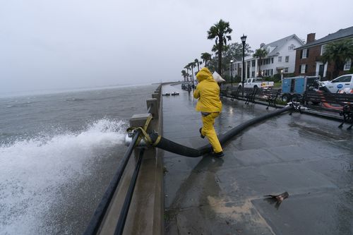 Pracownik przesuwa worek z piaskiem po umieszczeniu pompy, aby usunąć wodę z akumulatora, gdy czuje skutki huraganu Ian, piątek, 30 września 2022 r. w Charleston w Południowej Karolinie.