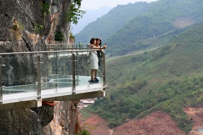 Visitors take photos on the walkway section of the Bach Long glass bridge in Moc Chau district in Vietnam's Son La province on April 29, 2022. - Vietnam launched a new attraction for tourists -- with a head for heights -- on April 29 with the opening of a glass-bottomed bridge suspended some 150 metres above a lush, jungle-clad gorge. (Photo by Nhac NGUYEN / AFP) (Photo by NHAC NGUYEN/AFP via Getty Images)