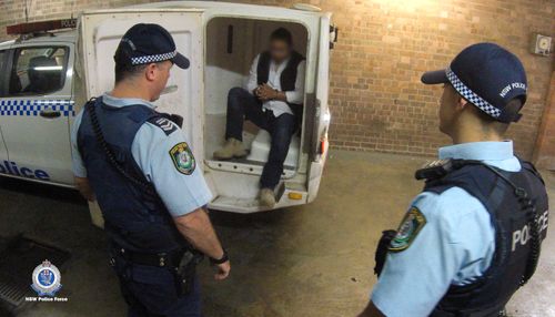 NSW Police escort an arrested Guatemalan man out of a police vehicle, following his arrest.