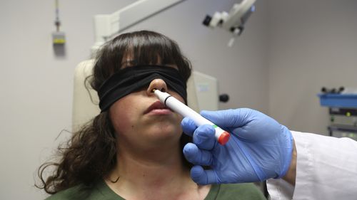 La mano de la Dra. Claire Vanderstein rocía un tubo de aroma debajo de la nariz de una paciente con los ojos vendados llamada Gabriella Forgione. 