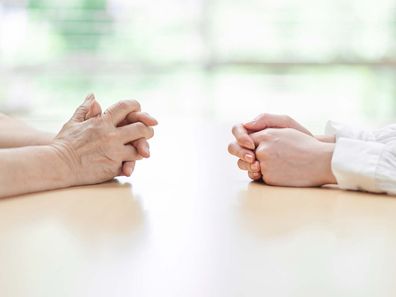 Two sets of hands resting in a table, on the left an elderly woman's and on the right a young woman's