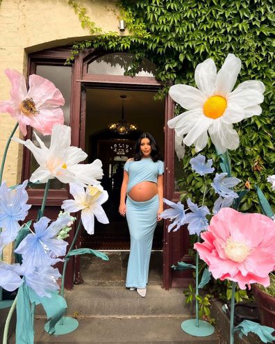 Inside Martha Kalifatidas' baby shower - Martha standing at an entrance surrounded  by huge flowers.