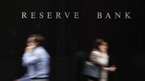 Two people on the phone walking in opposite directions outside the Reserve Bank of Australia, Sydney. The photo is taken with a deliberate blur.