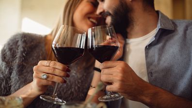Couple clink glasses with red wine at date in casual outfit in cafe. Couple having romantic moments.
