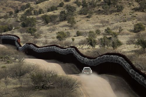 A Customs and Border Control agent patrols on the US side of a razor-wire-covered border wall along the Mexico east of Nogales, Arizona.