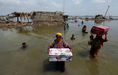 Women carry belongings salvaged from their flooded home after monsoon rains, in the Qambar Shahdadkot district of Sindh Province
