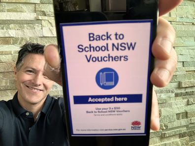 Liberal MP Victor Dominello holds up a phone showing Back to School NSW voucher scheme