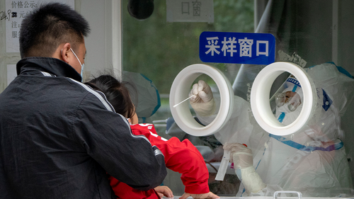 A worker in a protective suit swabs a childs throat for a COVID-19 test at a testing site in Beijing, Thursday, April 28, 2022. 