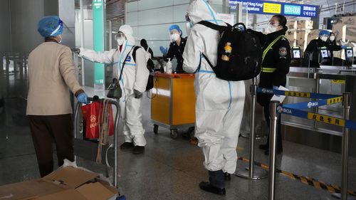 I passeggeri che indossano indumenti protettivi vengono indirizzati a un volo in un terminal dell'aeroporto di Pechino Capitale il 13 dicembre 2022. 