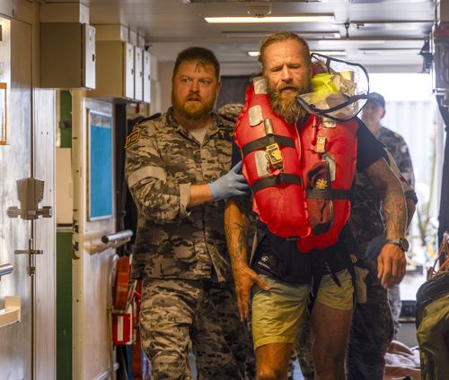 Chief Petty Officer Medic Peter Gough leads solo rowboat adventurer Aurimas Mockus to the ship's hospital onboard HMAS Choules.