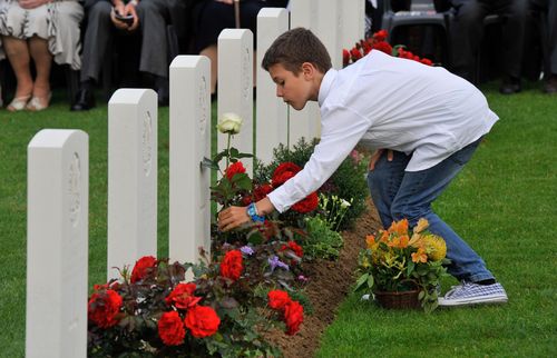 A French schoolboy lays a red rose on a soldier's grave during a Headstone Dedication Ceremony for Australian soldiers killed at Fromelles at the cemetery. The nine soldiers will be commemorated during a similar ceremony on July 19, 2018. (AAP)