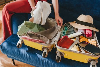 Beautiful smiling young woman packing personal belongings in a suitcase for travelling looking at list at tablet sitting on the sofa in the living room.