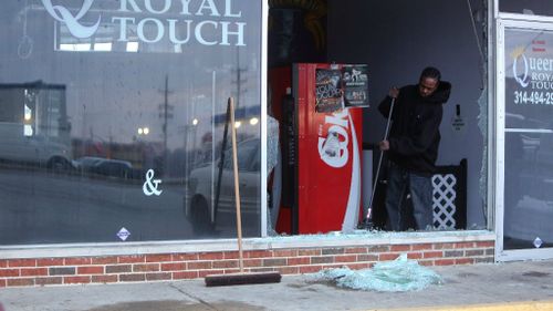 A man sweeps away glass and debris at his Ferguson hair dressing salon after rioters damaged the business. (AAP)