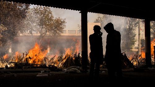 People are silhouetted against multiple burning funeral pyres of patients who died of COVID-19 in New Delhi, India.