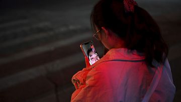 A woman makes a video call with a friend as she waits at an intersection to cross during rush hour on November 15 in Beijing, China.