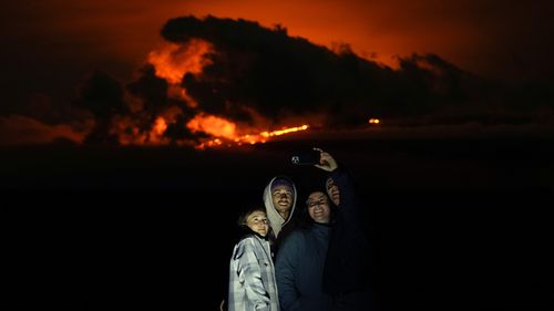 Ashlyn Nadeau, a sinistra, accanto a suo marito, Casey Nadeau, secondo da sinistra;  Jessica Doyle, la seconda da destra, e Justin Potter, a destra, mentre posano per una foto sotto il vulcano Mauna Loa mentre erutta venerdì 2 dicembre 2022, vicino a Hilo, Hawaii.