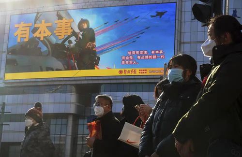Mieszkańcy w maskach na twarz czekają na przejście przez skrzyżowanie w pobliżu dużego ekranu promującego Siły Powietrzne Chińskiej Armii Ludowo-Wyzwoleńczej w Pekinie, poniedziałek, 9 stycznia 2023 r. Chińskie wojsko przeprowadziło wspólne ćwiczenia ofensywne na dużą skalę, które rozpoczęły się w niedzielę , i wysłał samoloty bojowe i okręty wojenne w kierunku Tajwanu, według chińskich i tajwańskich ministerstw obrony.  (Zdjęcie AP/Andy Wong)