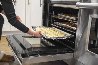 A Caucasian woman is putting delicious food on a tray in the oven to cook it for her family's Thanksgiving dinner.  The oven is a large stainless steel double gourmet oven with large red knobs.  There's more food in the oven.  Taken with a Canon 5D Mark 3. rm