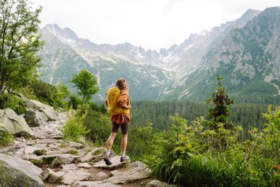 Happy woman with a yellow hiking backpack enjoying the mountain landscape. A young traveler travels along mountain paths. Adventure, travel concept.