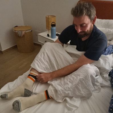 Man puts on socks while sitting in bed.