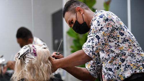 Hairdresser colours a customer's hair wearing a face mask. 