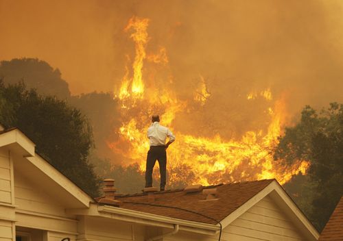 A man on a rooftop looks at approaching flames as the Springs fire continues to grow in 2013, near Camarillo, California. 